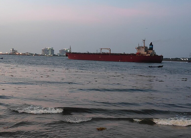 A large red cargo ship on calm waters with a city skyline in the background. 5