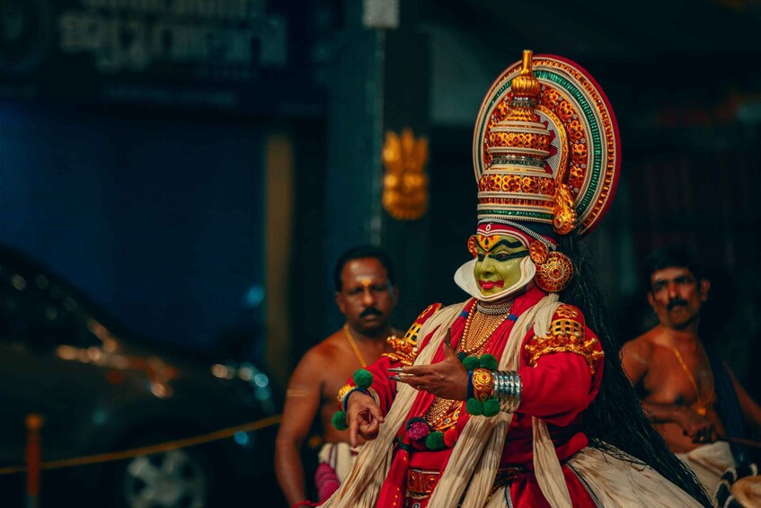A person in traditional attire with a large ornate headdress, holding a small object. 1