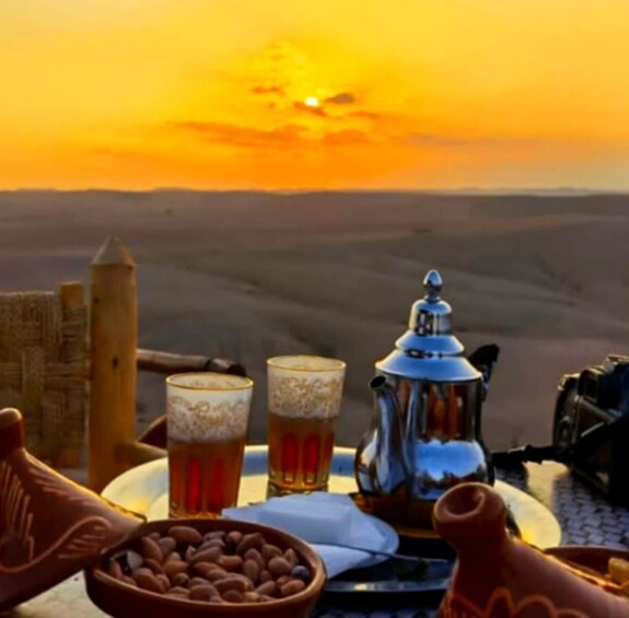 A desert sunset with a table set for tea, including a teapot, cups, and a bowl of nuts. 4