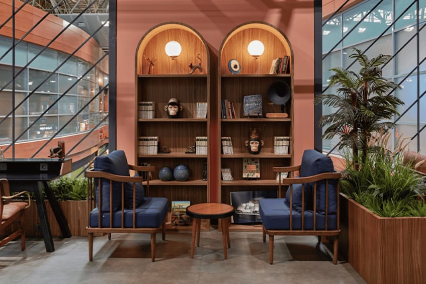 A cozy reading area with two blue armchairs, a small round table, and wooden bookshelves with various decorative items. 3