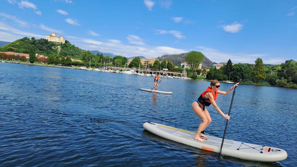 Two people paddleboarding on a calm lake with a cityscape and hills in the background. 5