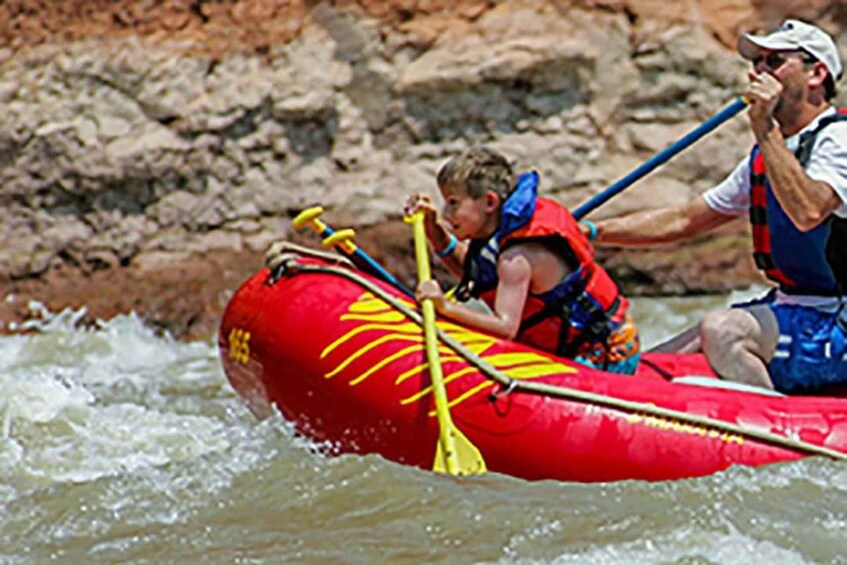 A red inflatable raft with yellow paddles, a person wearing a life jacket, and another person in a white cap. 2