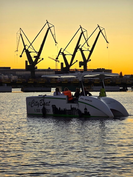A boat with 'eCityBoat' and 'POL 000K2G' on its side, docked at a port with cranes in the background during sunset. 4