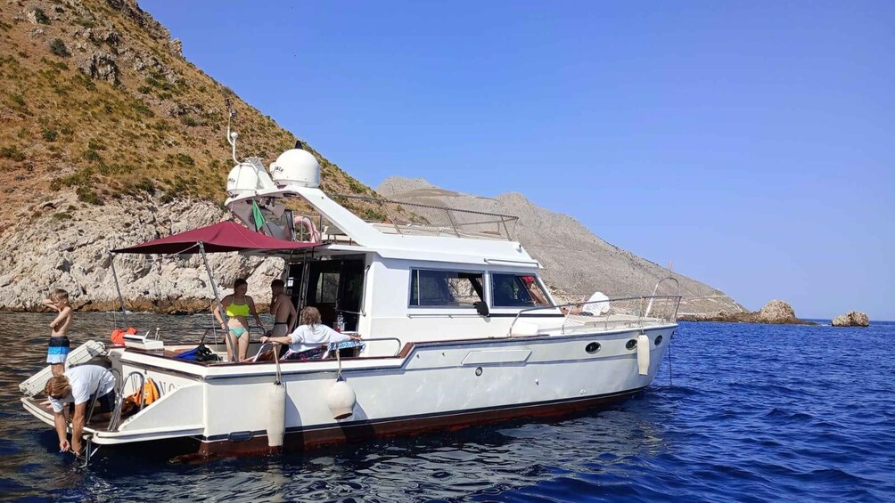 A white boat with a red canopy on a calm sea, rocky cliffs in the background, and a clear sky. 2