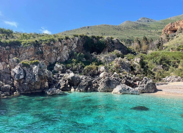 A coastal landscape with clear turquoise waters, rocky cliffs, and a mountainous backdrop. 5