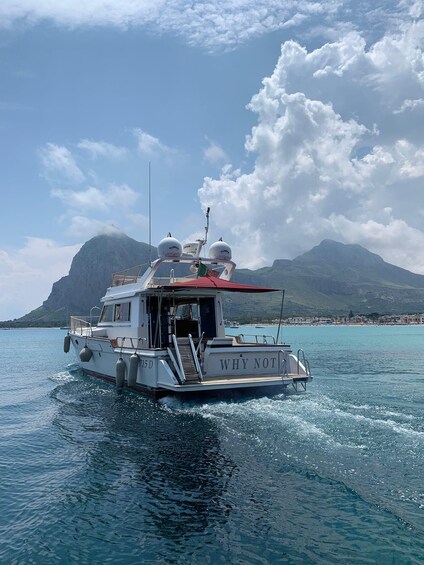 A white boat with 'WHY NOT' on the bow, sailing on turquoise water with a mountainous backdrop. 4