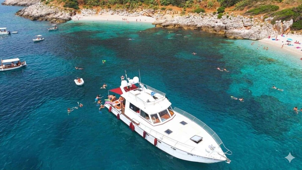 A boat with people swimming around it in clear waters near a rocky coastline. 1