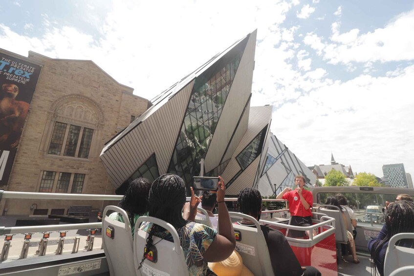 A group of people on a bus with a building featuring a large glass facade in the background. 4