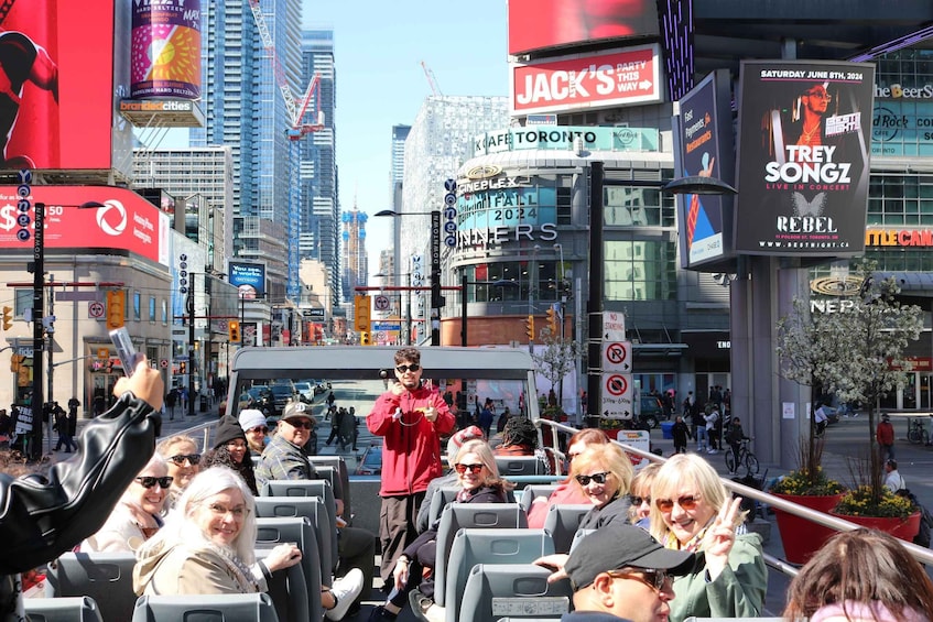 A busy urban street with a bus filled with passengers, surrounded by tall buildings and various advertisements. 1