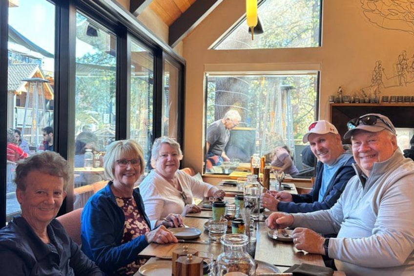 A group of people sitting around a table in a restaurant with large windows and a wooden ceiling. 5