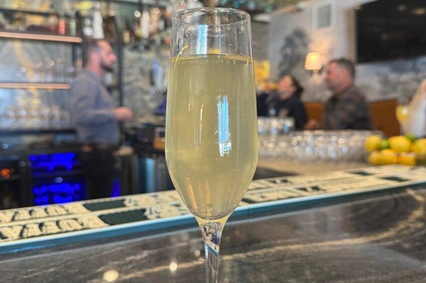 A glass of white wine on a bar counter with a blurred background of people and bar shelves. 3