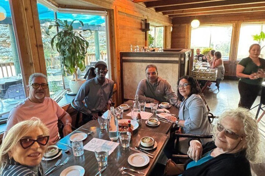 A group of people dining at an outdoor restaurant with wooden tables and potted plants. 2