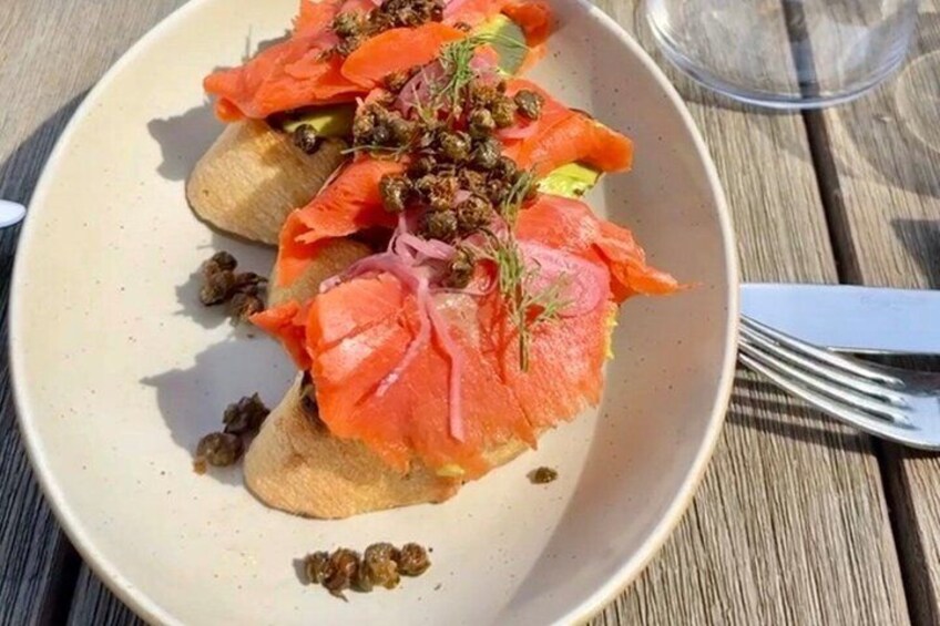 A plate of food with salmon, capers, and a garnish on a wooden table. 3