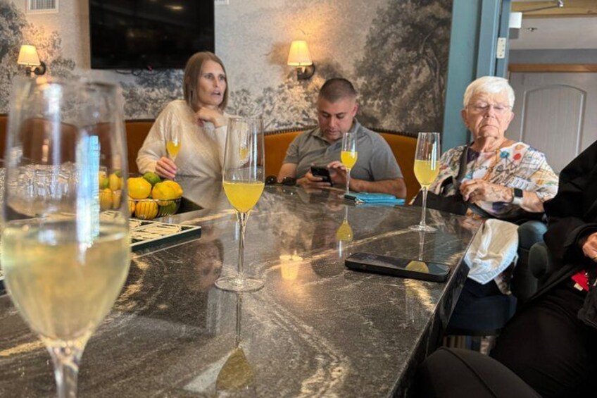 A group of people seated at a table with glasses of wine and lemons. 2