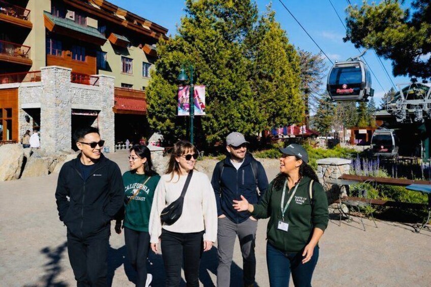 A group of people walking on a paved path with buildings and a ski lift in the background. 1