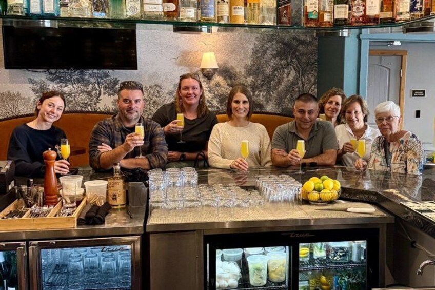 A group of people sitting at a bar with drinks and a refrigerator filled with bottles. 5