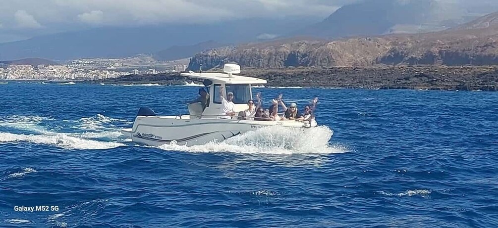 A boat with passengers on a clear day, moving through blue water with a coastal landscape in the background. 5