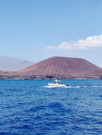 A boat on a blue sea with a mountain in the background. 3