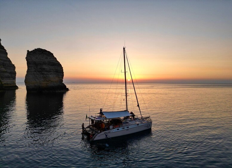 A sailboat anchored near a rocky coastline during sunset. 1