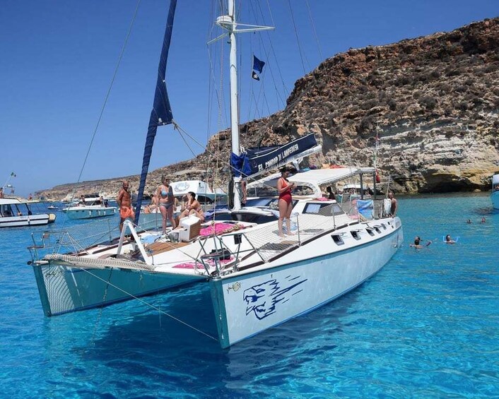 A sailboat docked at a marina with people on board and swimmers in the water. 3