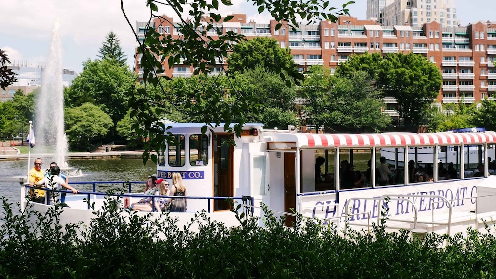 A riverboat with 'Charles Riverboat Co.' on the side, docked near a fountain, with buildings and trees in the background. 3