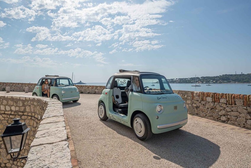 Two vintage cars parked on a stone-paved area by the sea. 1