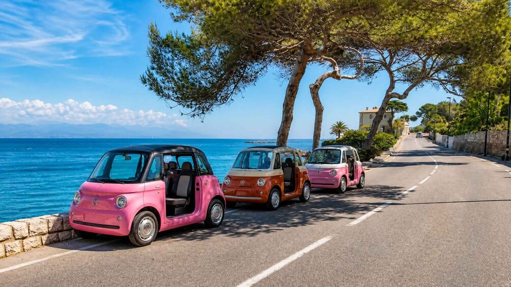 Three vintage cars parked on a coastal road with a clear view of the sea and a stone wall on one side. 1