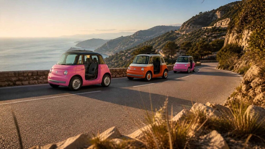 Three small cars on a winding coastal road with a mountainous backdrop. 4