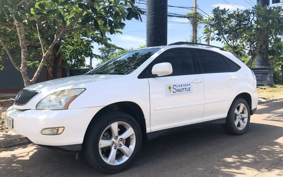 A white SUV parked on a street with trees and a utility pole in the background. 2