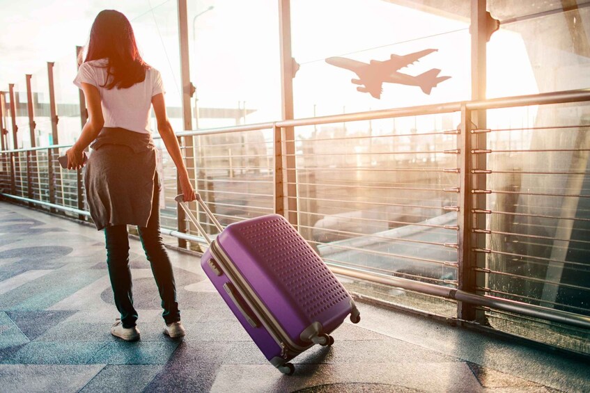 A person with a purple suitcase standing on a tiled surface near a window with a silhouette of an airplane. 2