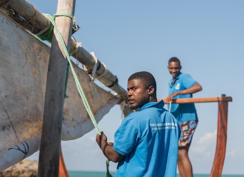 Two individuals in blue shirts working on a boat, with a clear blue sky in the background. 5