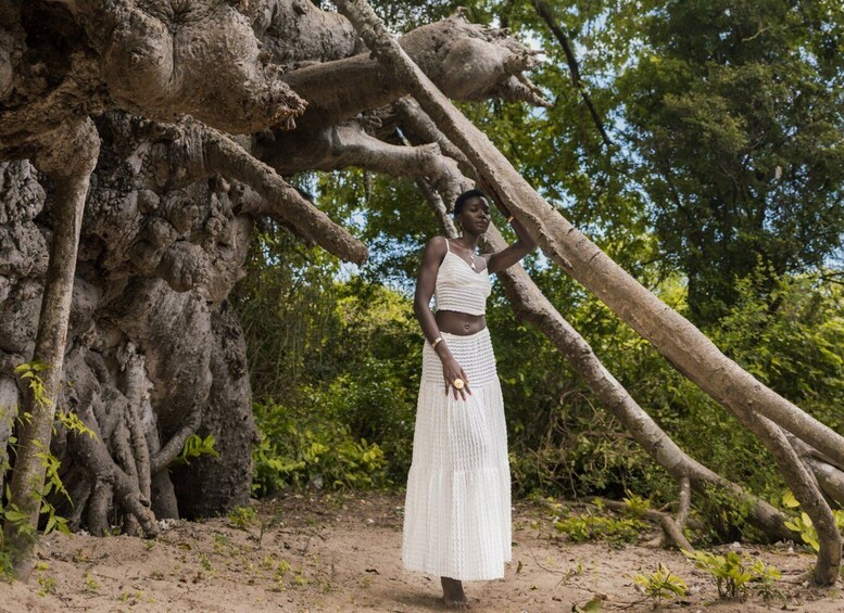 A person standing next to a large tree with thick roots and branches. 4