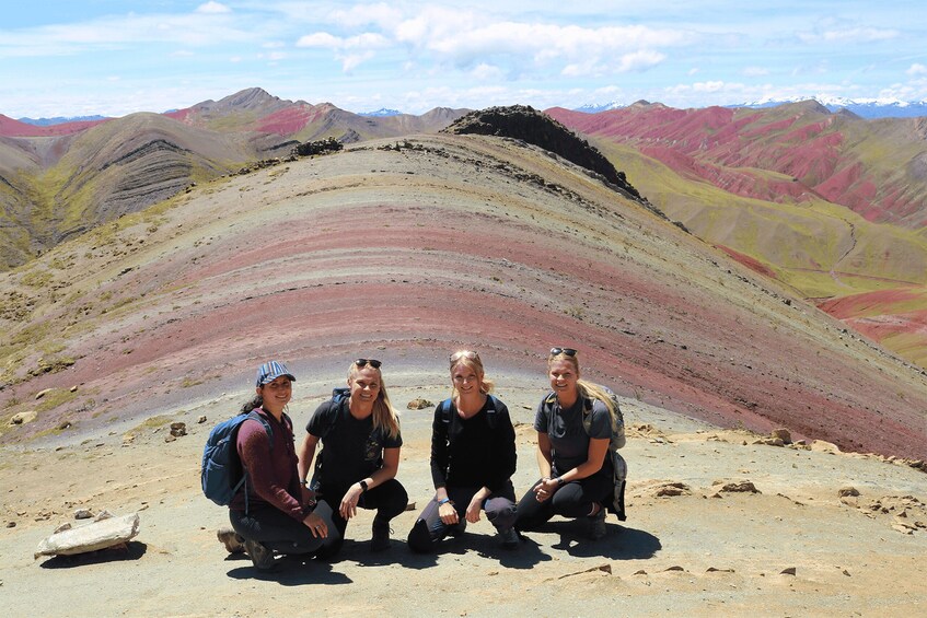 Four people posing on a mountain ridge with colorful rock formations in the background. 2