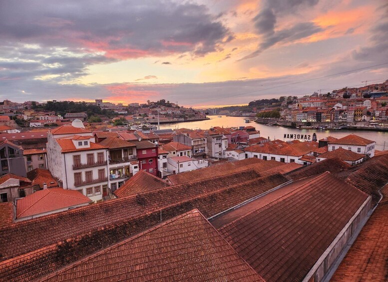 A coastal cityscape with terracotta-roofed buildings, a river, and a sunset sky. 5