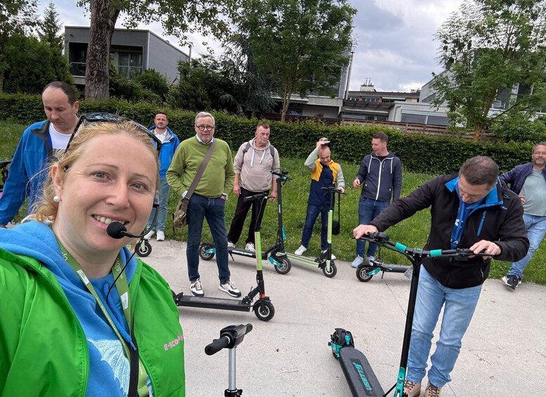 A group of people on electric scooters in an outdoor setting with trees and buildings in the background. 1