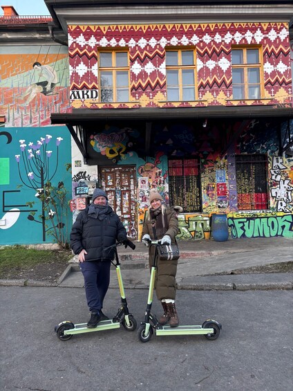 Due persone su scooter elettrici di fronte a un edificio con graffiti colorati e un murale. 2