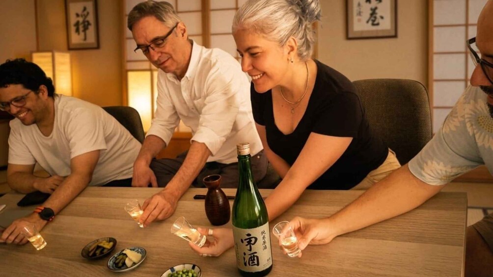 A group of people sitting around a table with a bottle of sake and glasses. 1