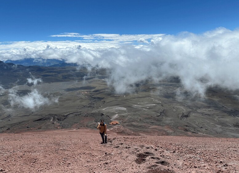A person standing on a rocky terrain with a view of a vast landscape and clouds above. 1