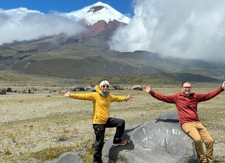 Two people standing on rocks with a snow-capped mountain and clouds in the background. 3