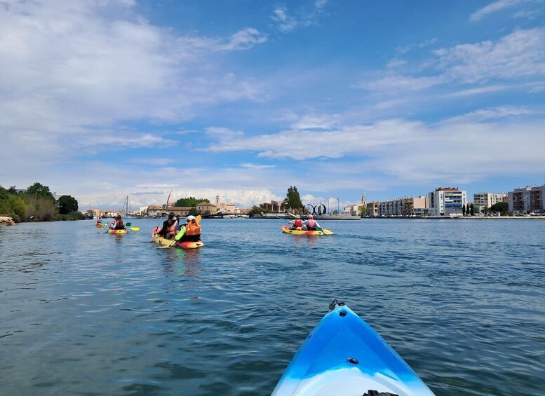 A group of kayakers on a calm river with buildings in the background. 3