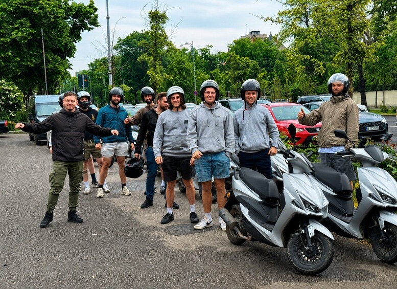 A group of people with helmets standing next to a scooter on a street. 2