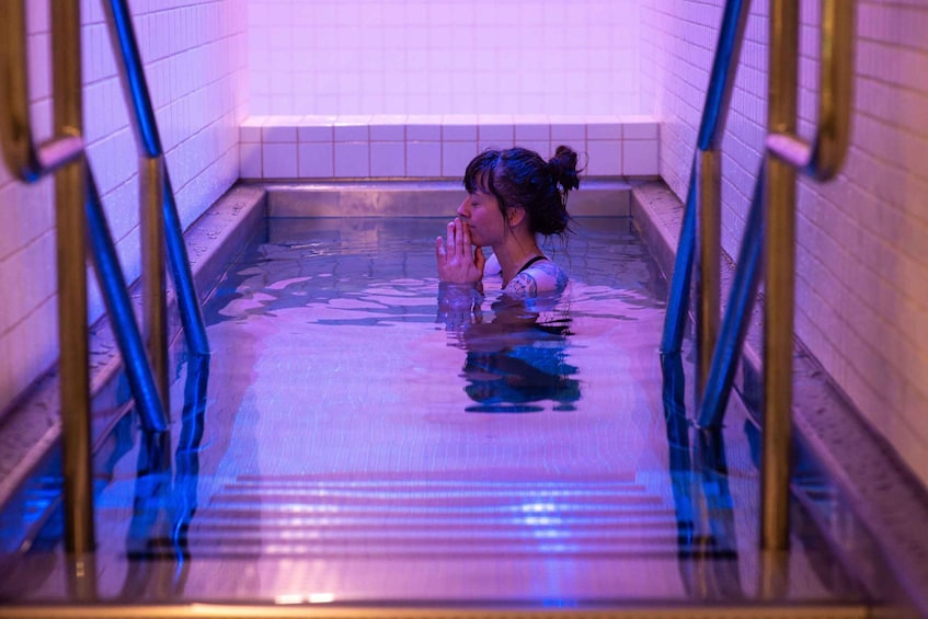 A person in a swimming pool with tiled walls and metal railings. 4
