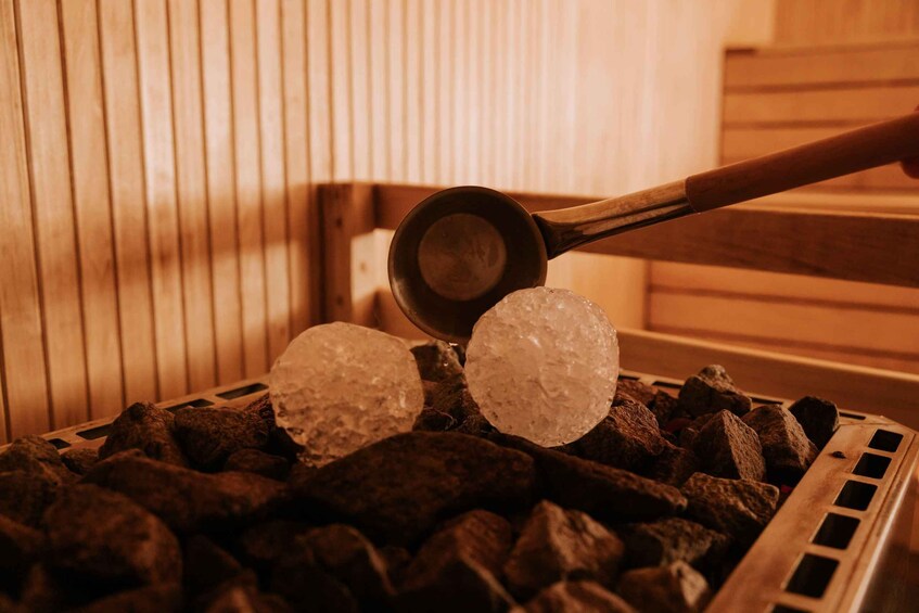 A wooden sauna with a metal ladle holding ice cubes over charcoal. 5