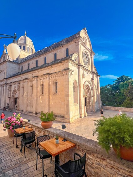 A historic building with a dome and clock tower, outdoor seating with potted plants, and a clear blue sky. 2