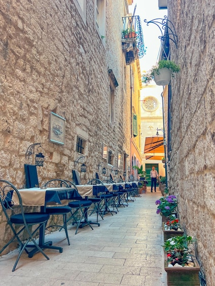 A narrow street with outdoor seating, stone walls, and potted plants. 1