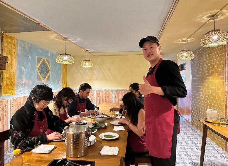A restaurant interior with diners, a waiter, and a large pot on the table. 2