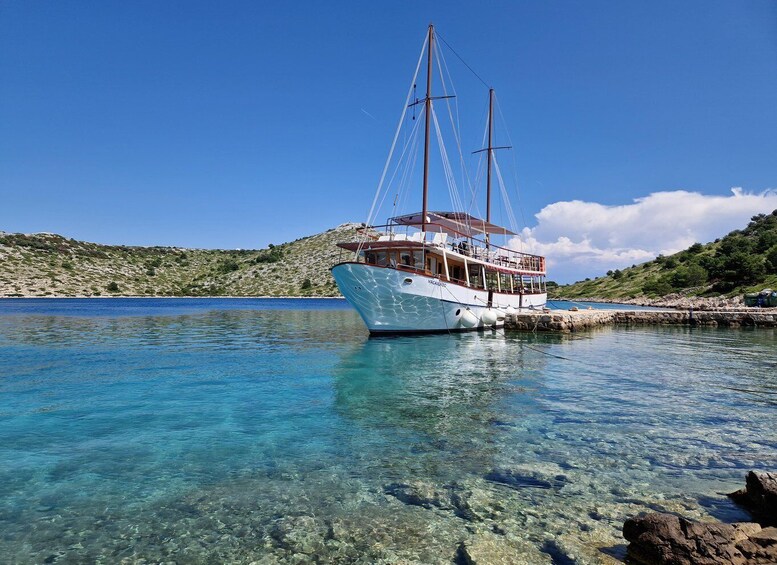 A sailboat named 'VAGABUNDO' anchored near a rocky shoreline with clear blue water. 1