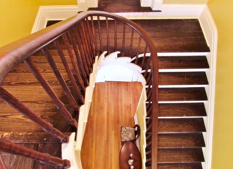 A wooden staircase with a handrail, white steps, and a wooden banister. 1