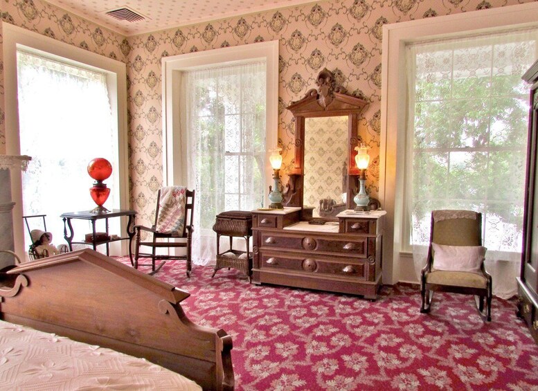 A vintage bedroom with floral wallpaper, a wooden dresser, a red patterned carpet, and a billiards table. 5