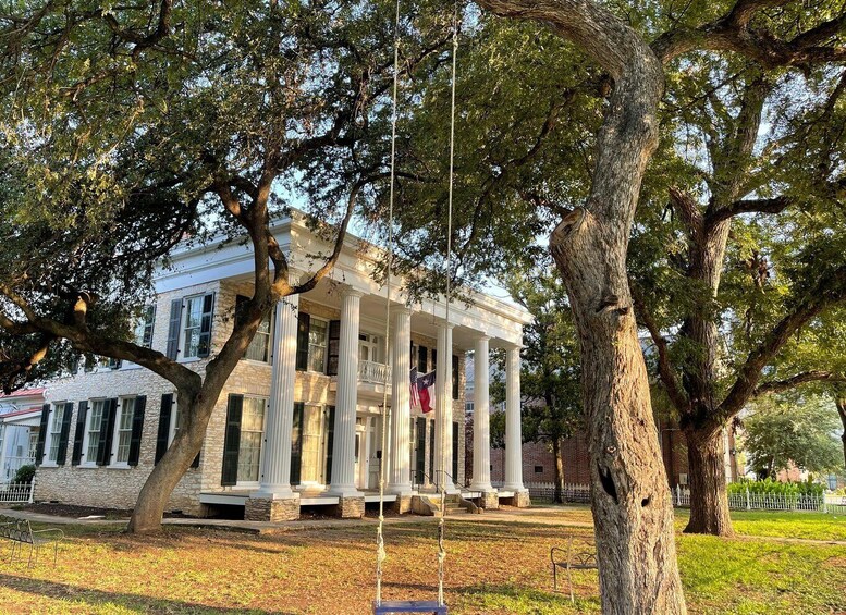 A historic building with columns and a flag, surrounded by trees and grass. 2
